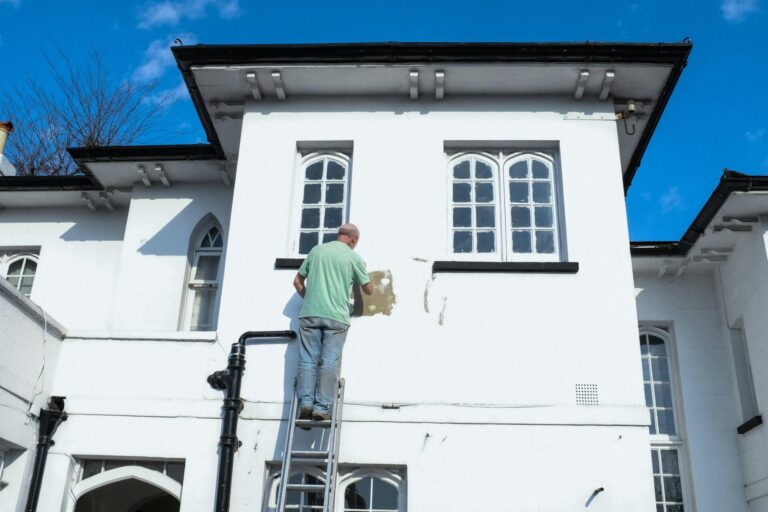 Man painting white queenslander house exterior on a ladder